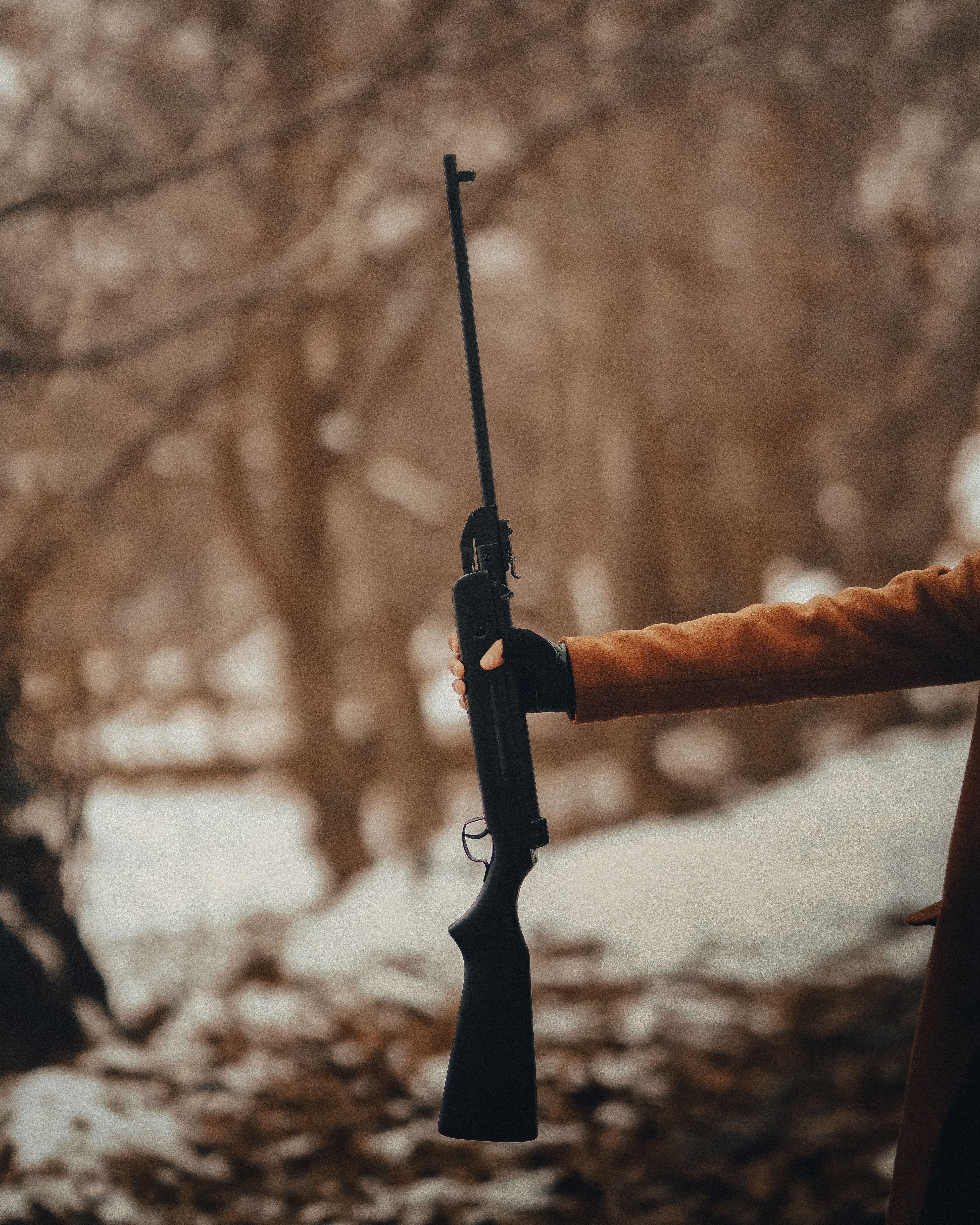 A break-action long gun held up against a snowy winter forest backdrop.