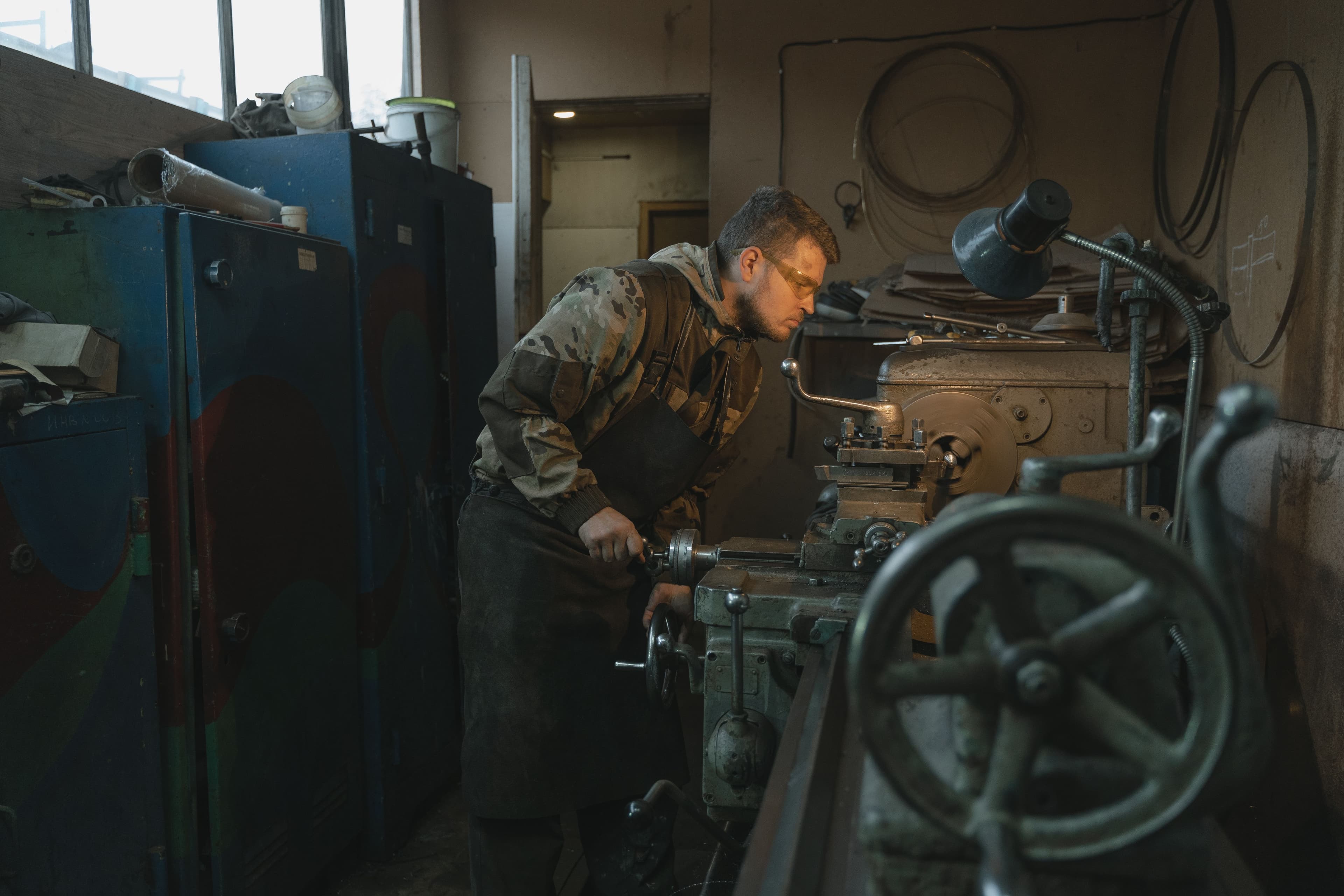 A gunsmith wearing safety glasses operates a metal lathe in a workshop.