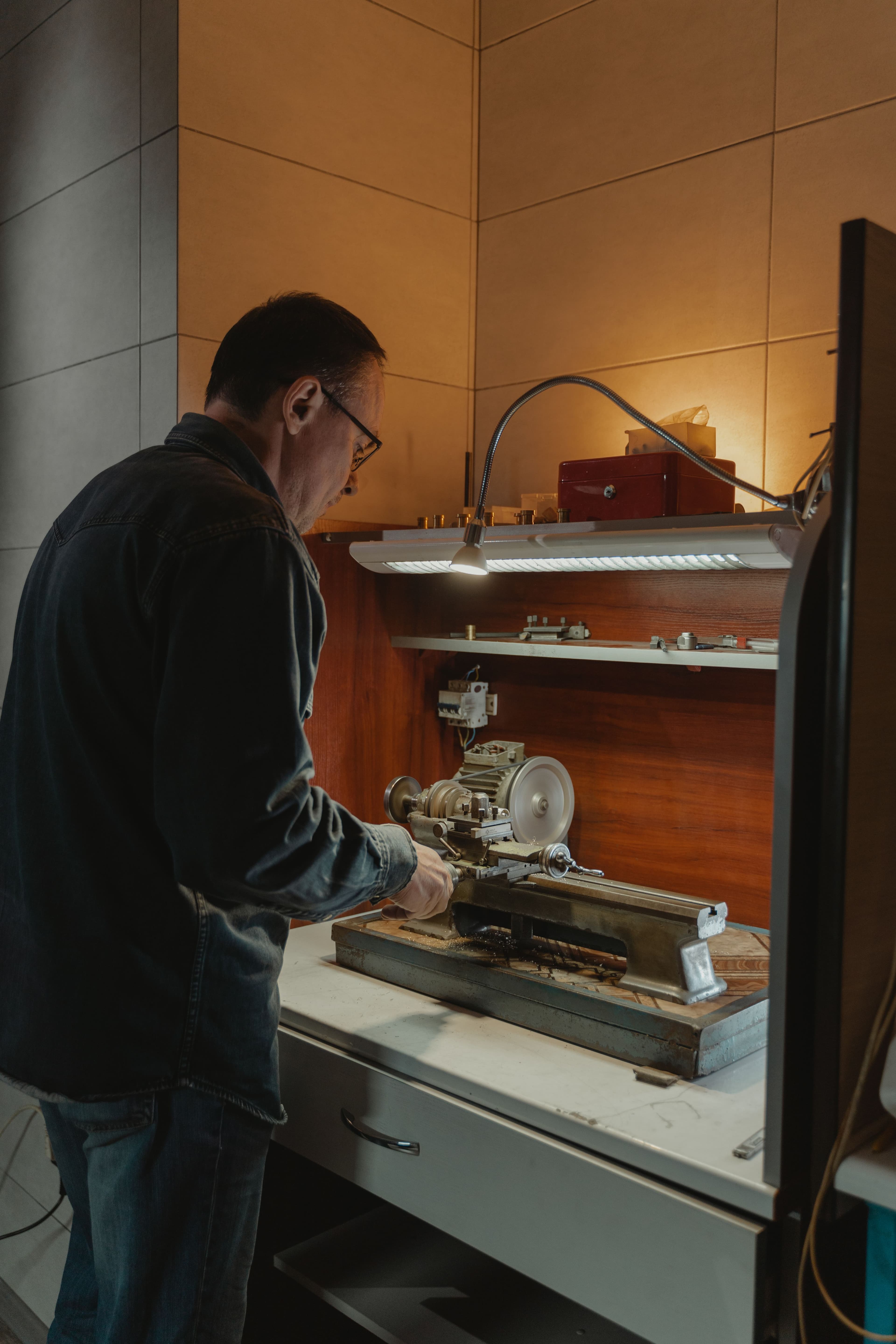 A craftsman operates a small metal lathe at a workbench.