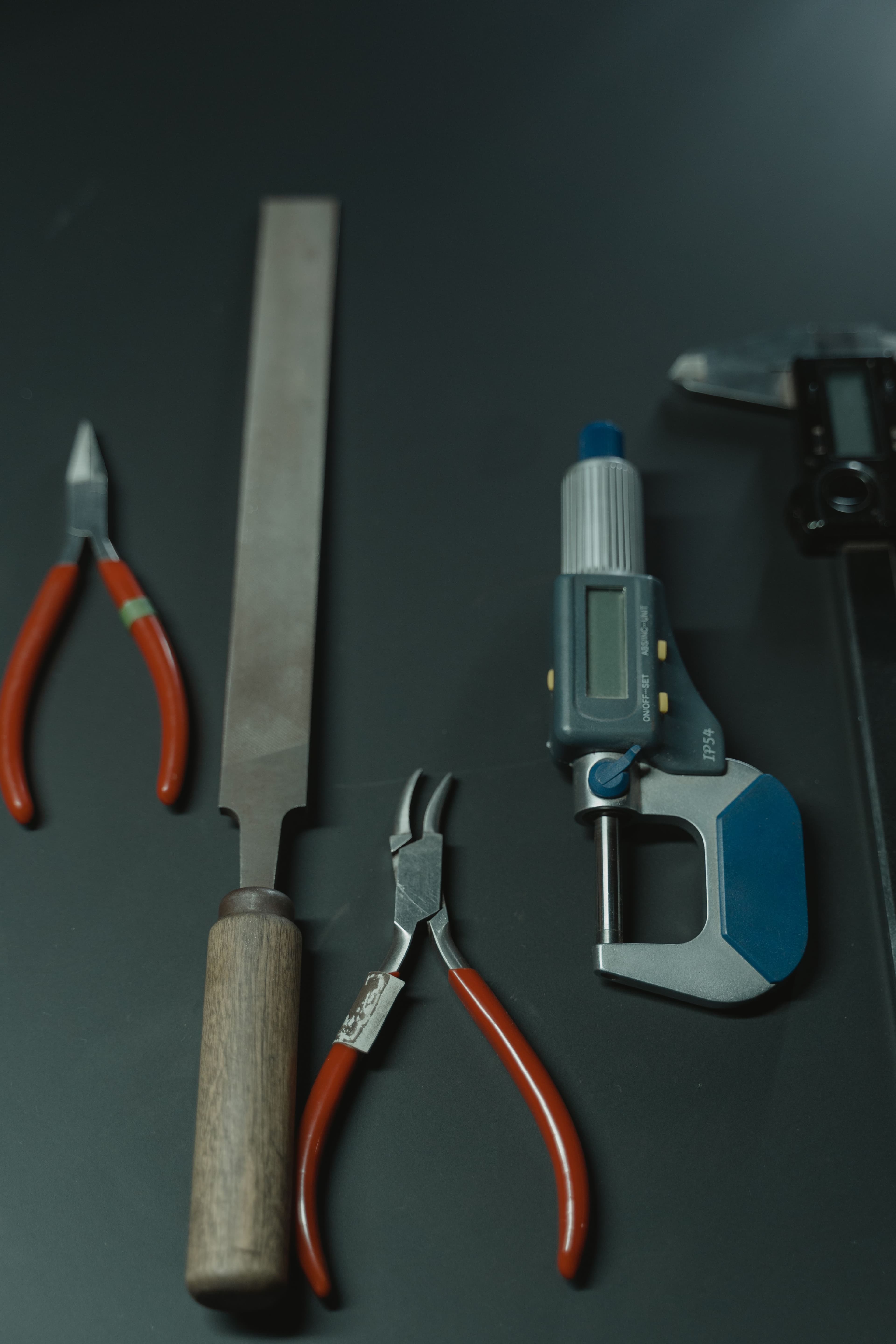 Flat lay of gunsmithing hand tools including pliers, a file, and a caliper.
