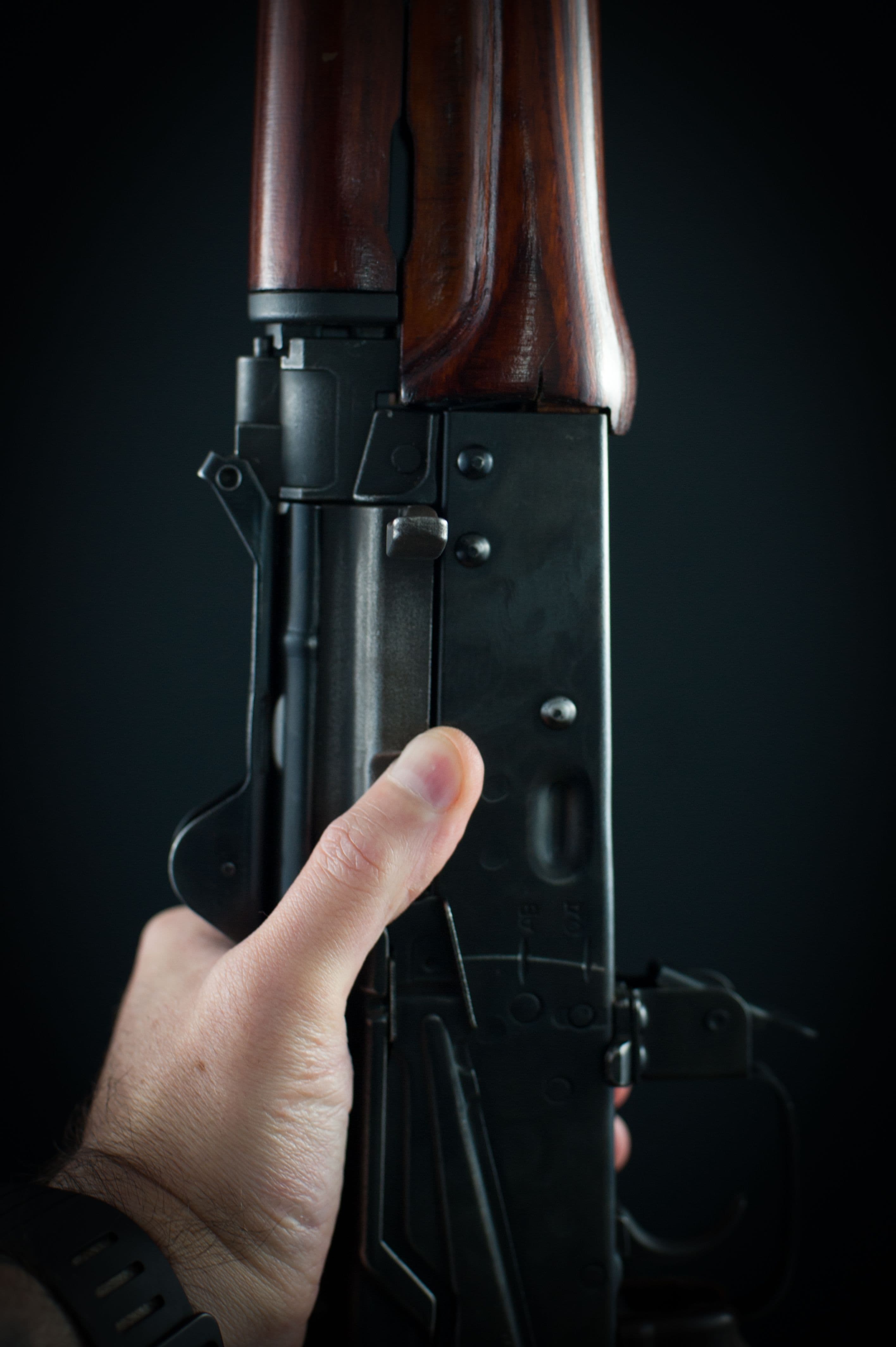 Close-up of a hand operating the selector lever on a wood-stocked rifle.