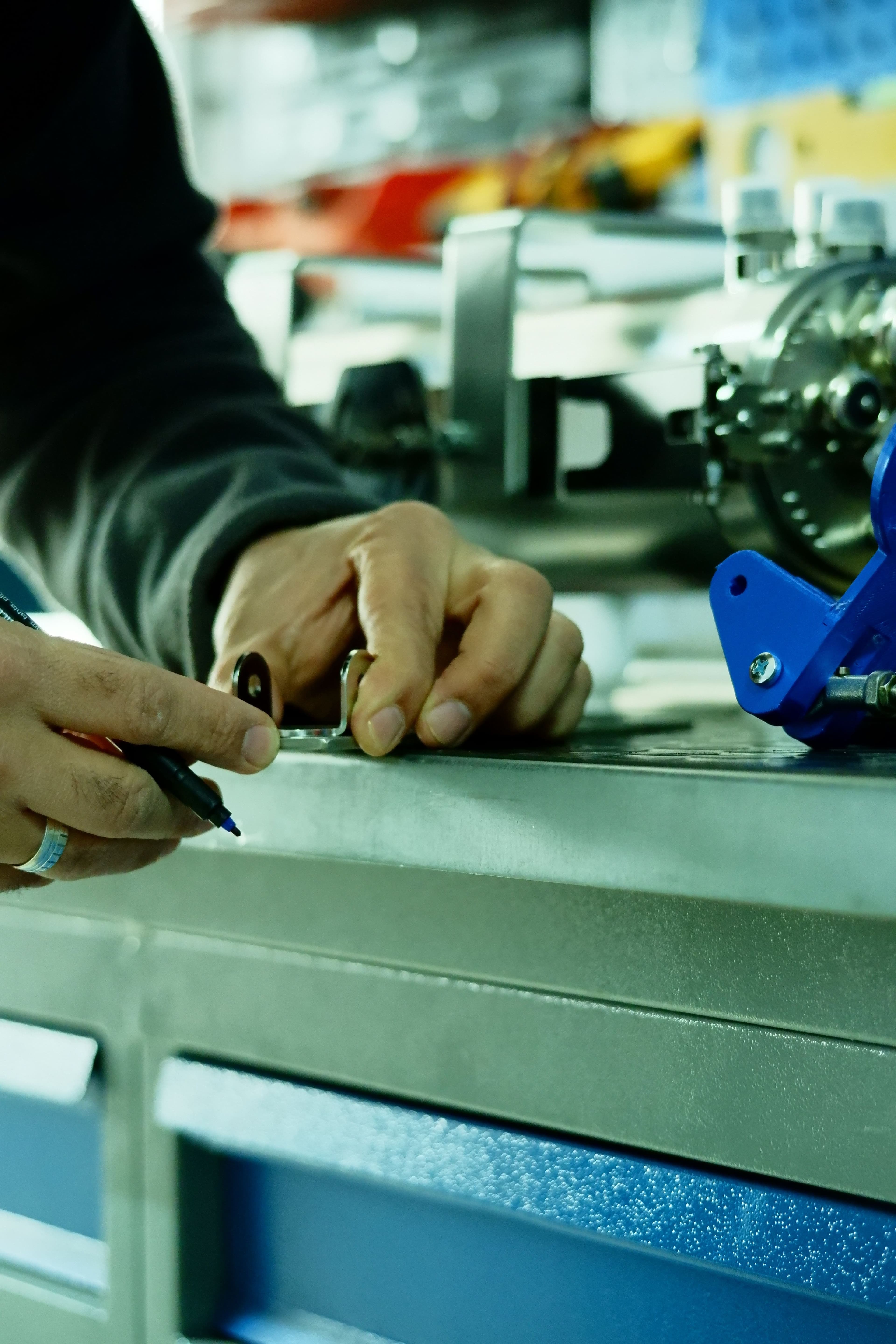 Hands marking a small metal bracket on a workshop bench.