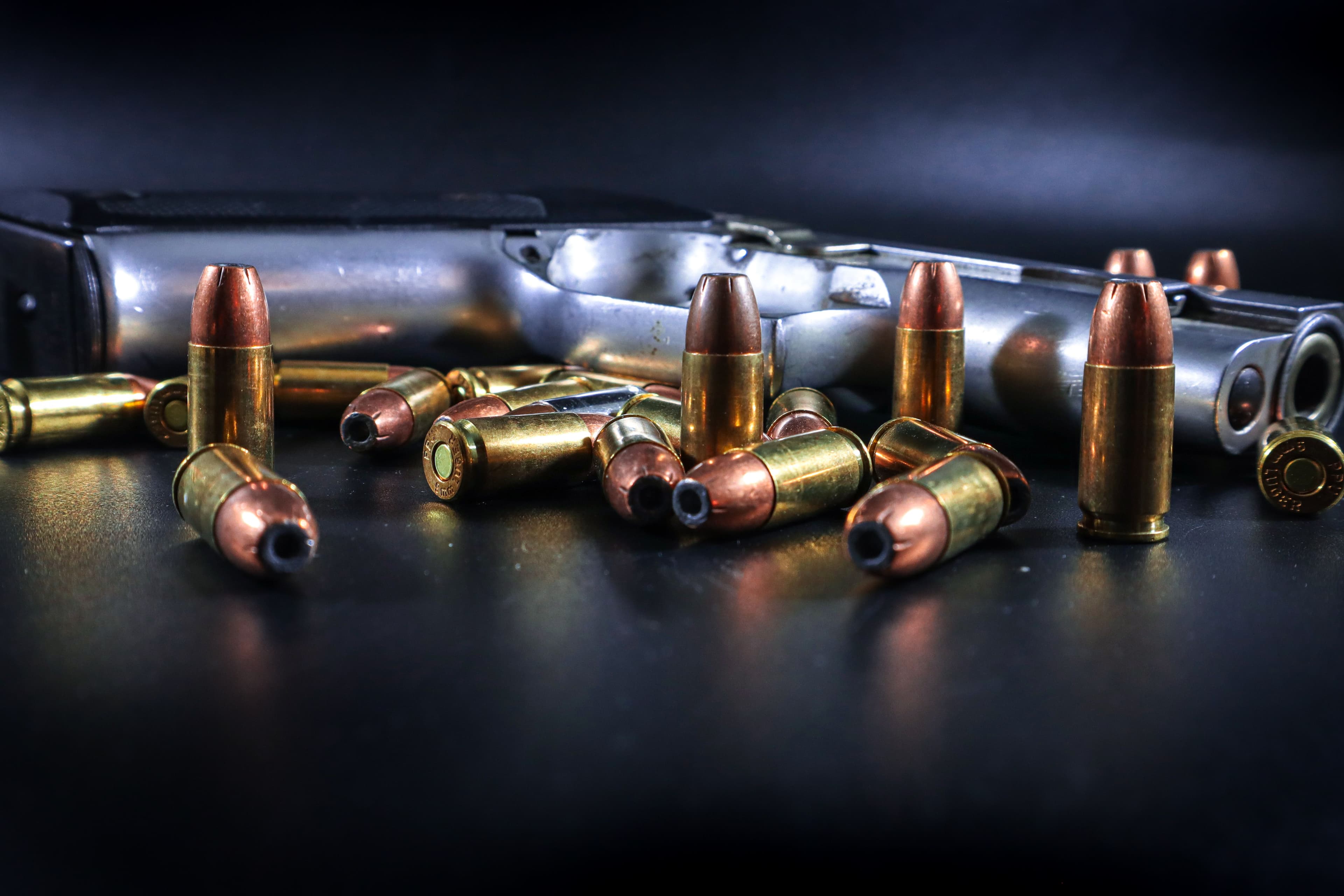 Hollow point pistol cartridges piled beside a handgun in studio light.