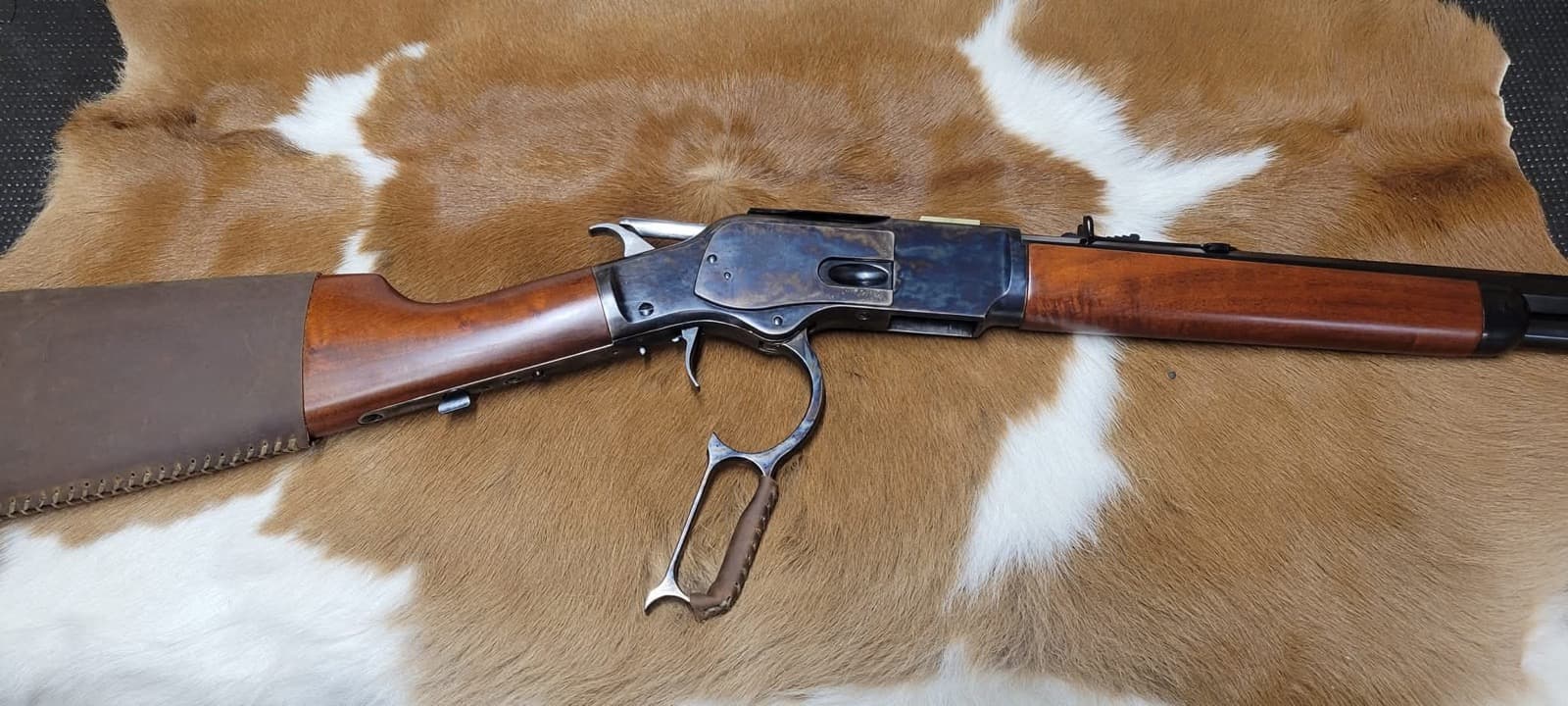 A lever-action rifle with a case colored receiver resting on a hide, serviced for cowboy action shooting