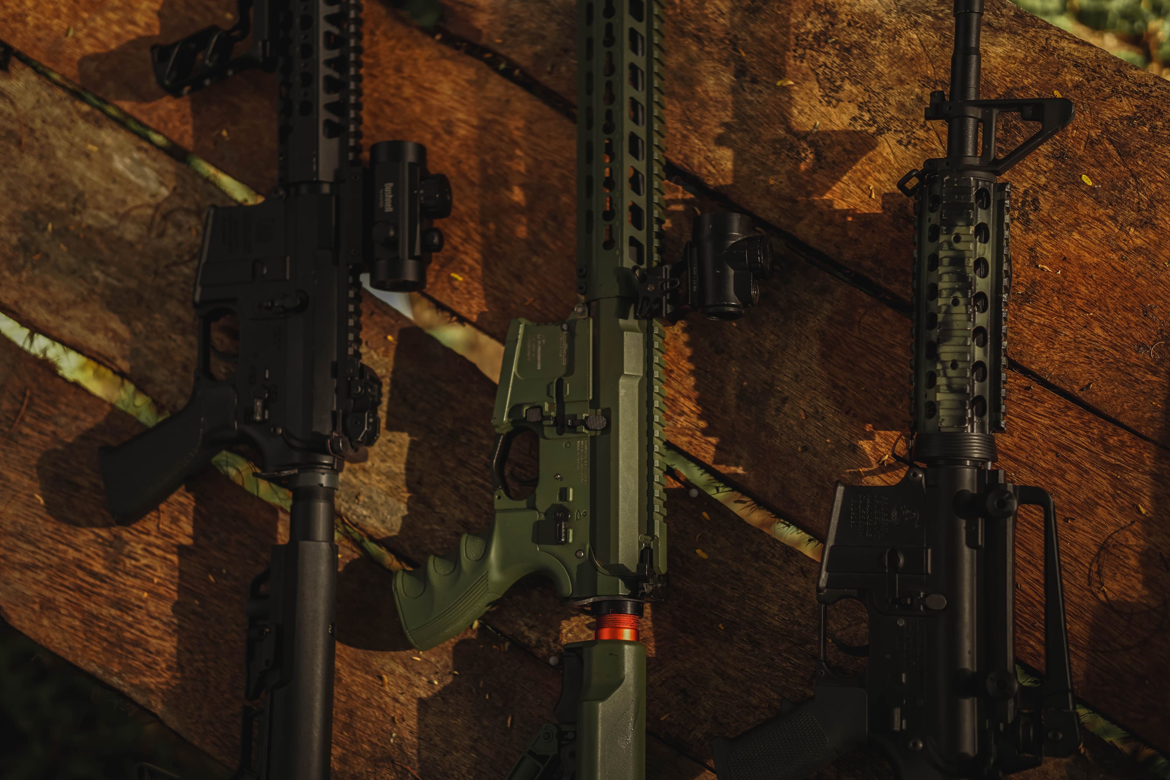 Several modern sporting rifles with optics laid out on a wooden surface.