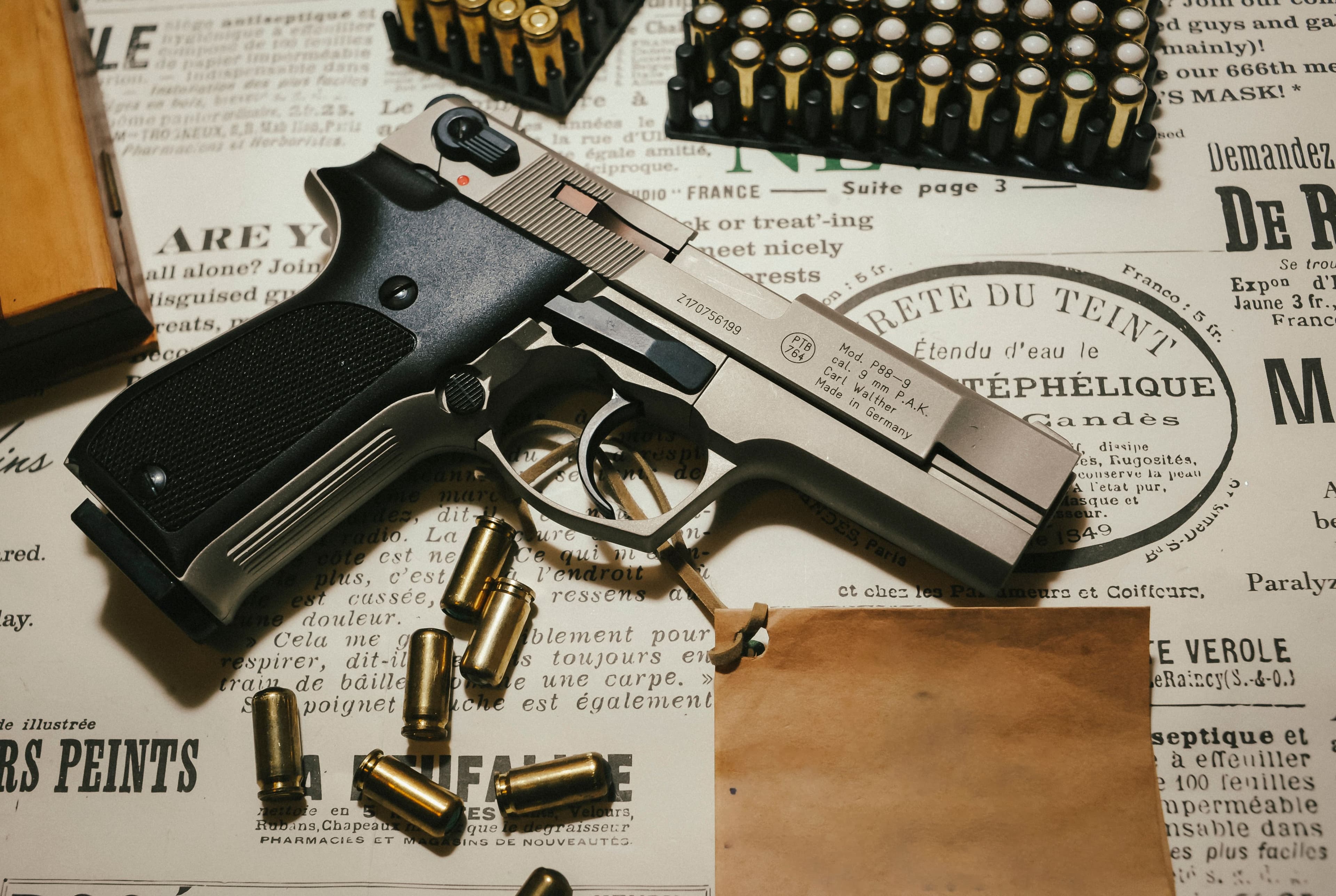 A pistol displayed with loose ammunition on a vintage paper backdrop.