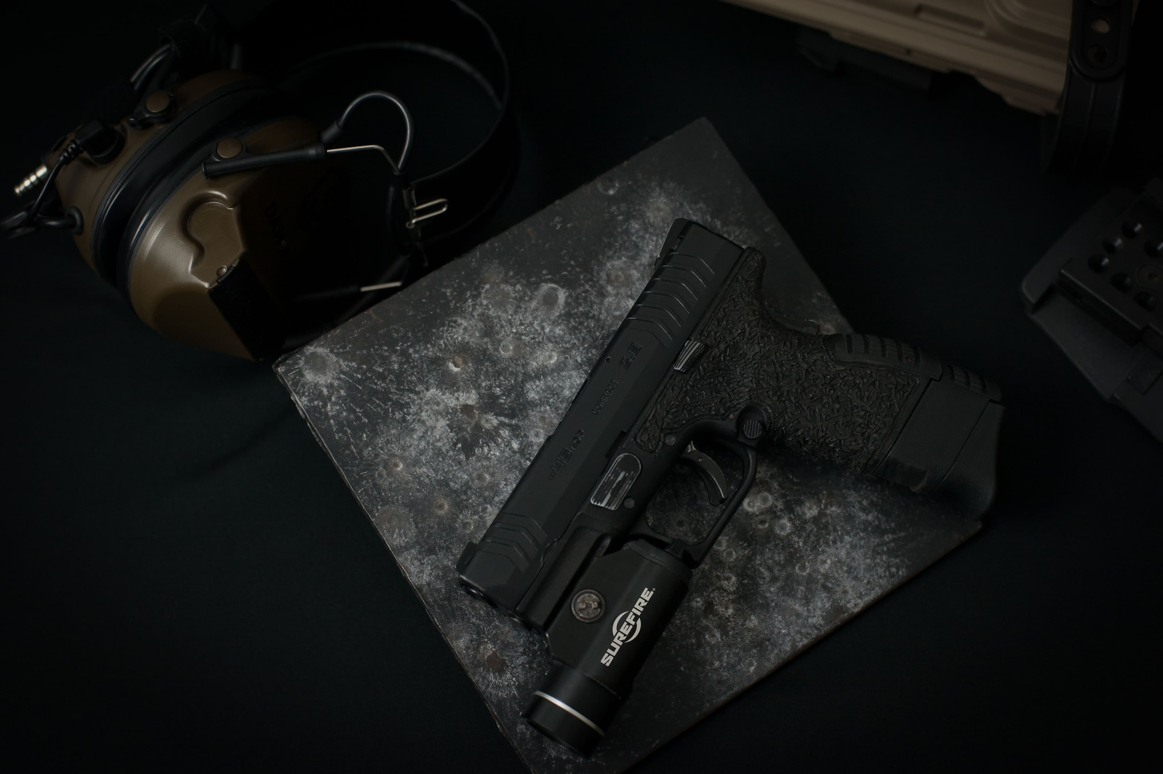 Pistol fitted with a tactical weapon light beside shooting ear protection.