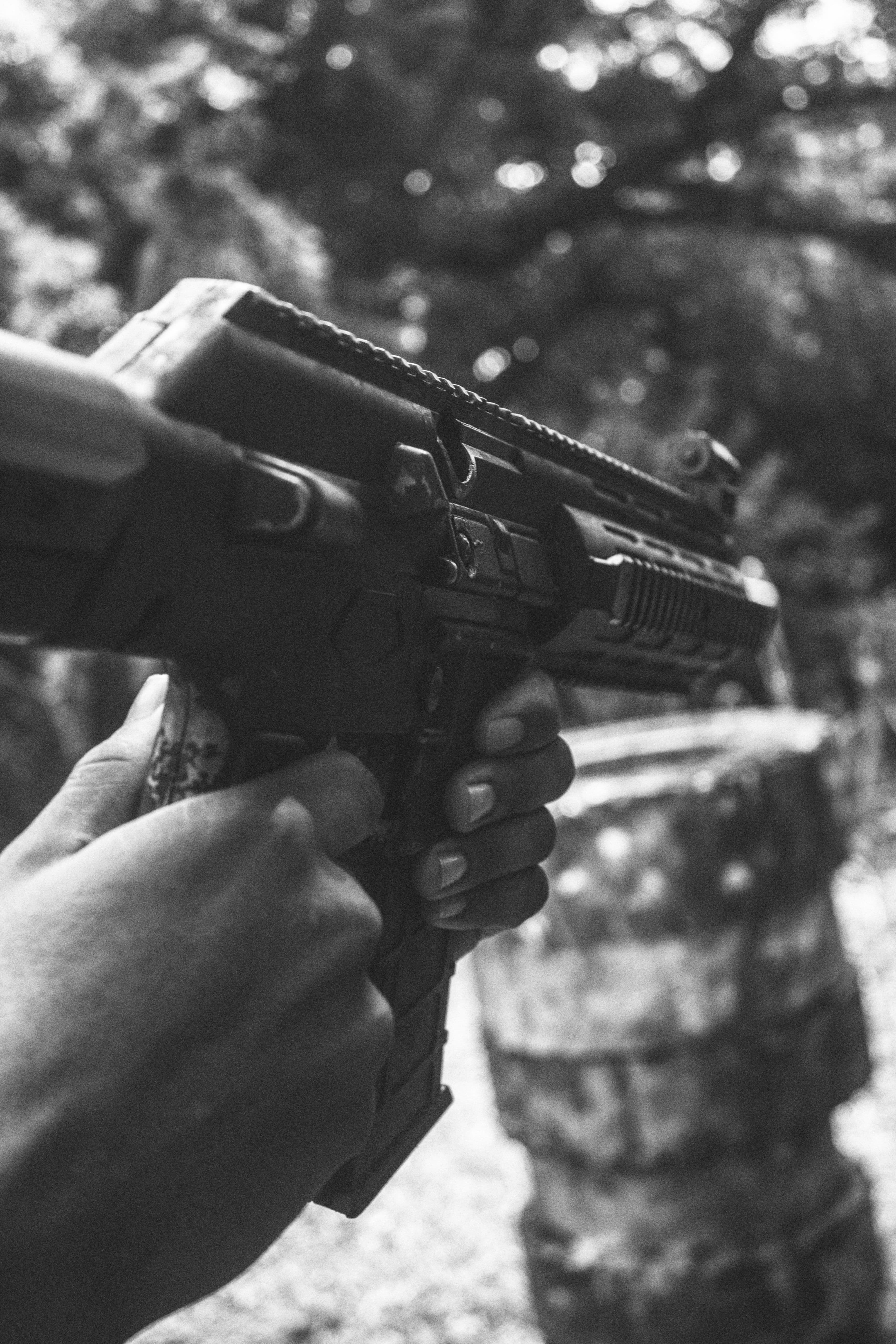 Black and white photo of a rifle fitted with a red dot sight held outdoors.