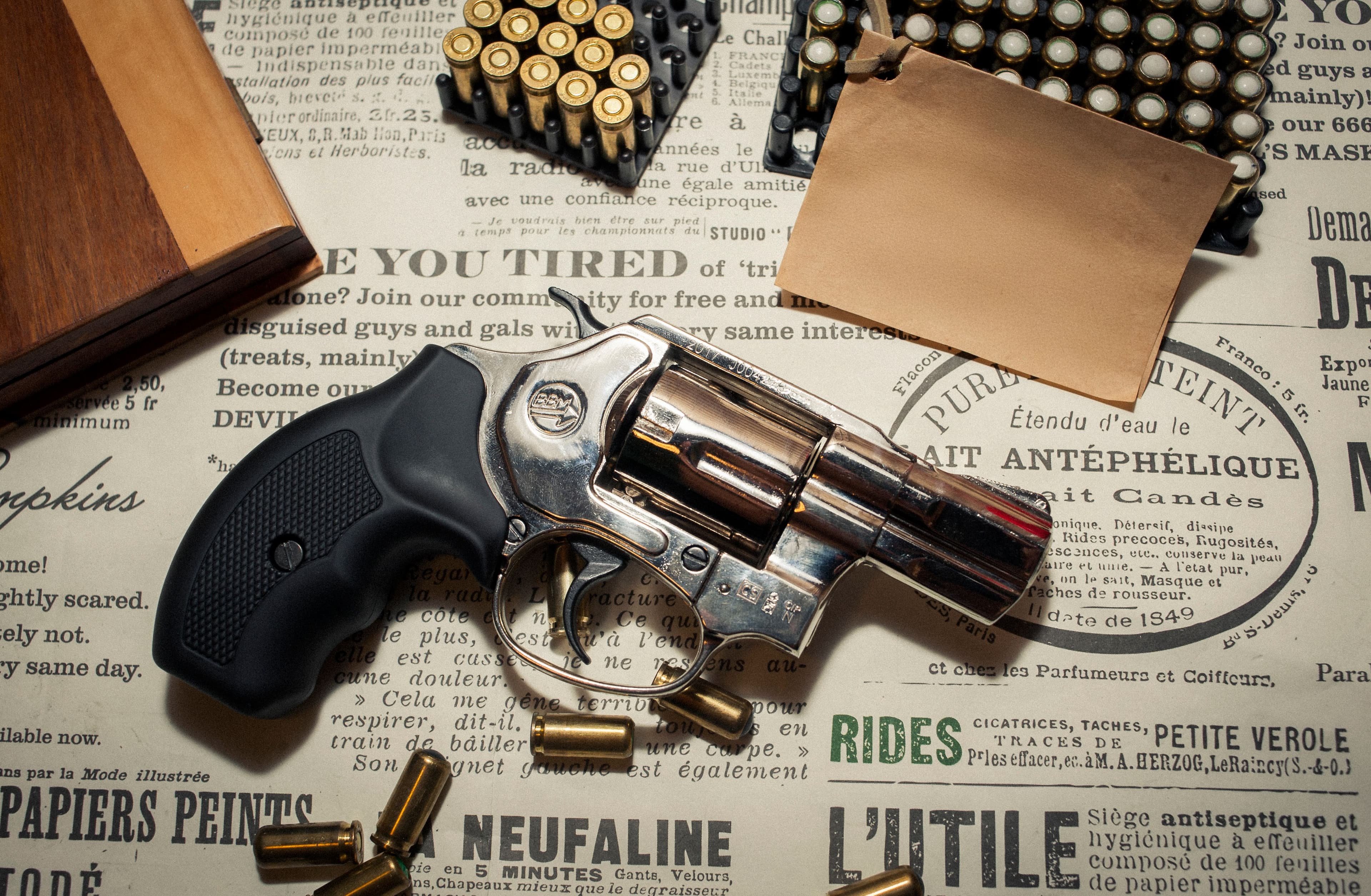 A revolver displayed among ammunition on a vintage paper backdrop.