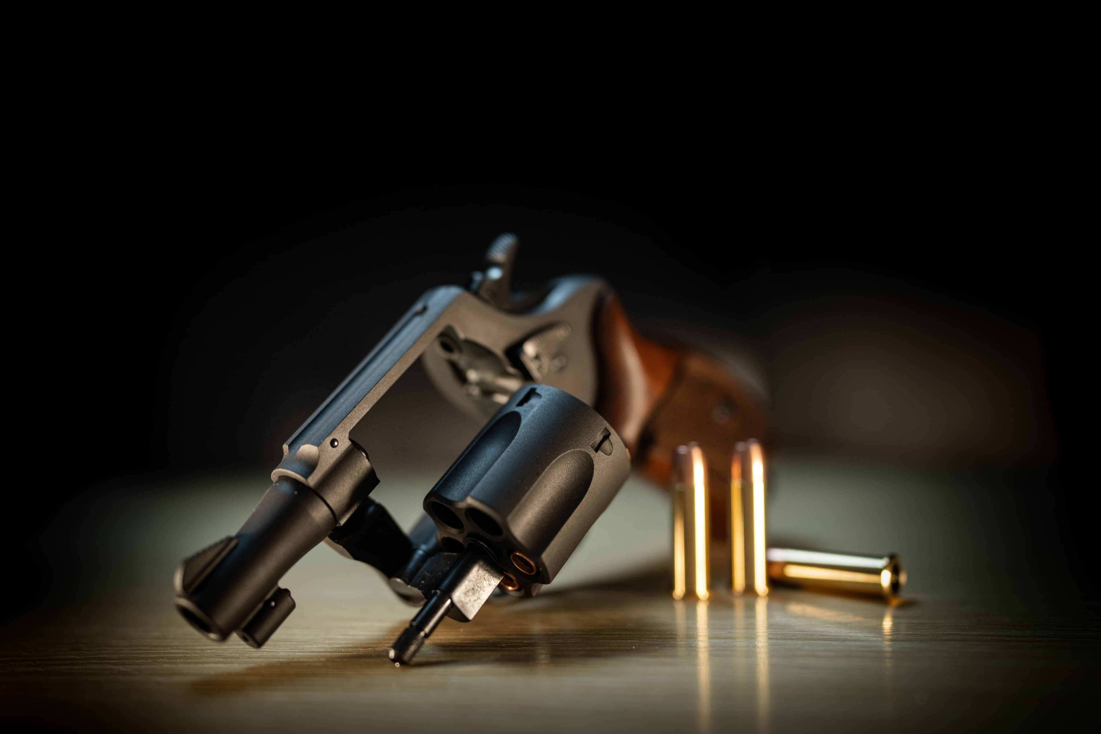 An open revolver cylinder rests on a table beside loose cartridges.