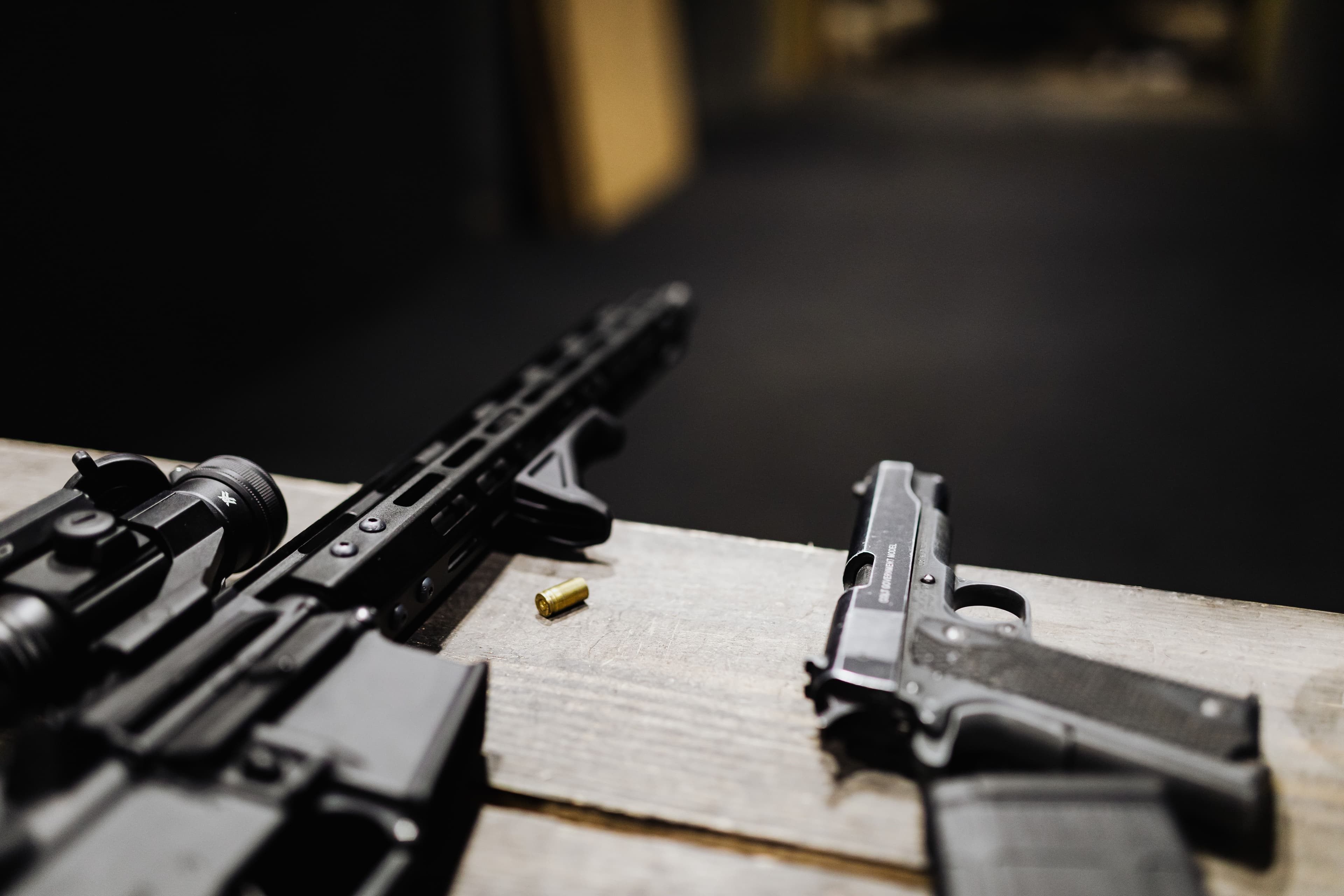 Close-up of a rifle handguard and pistol resting together on a range bench.