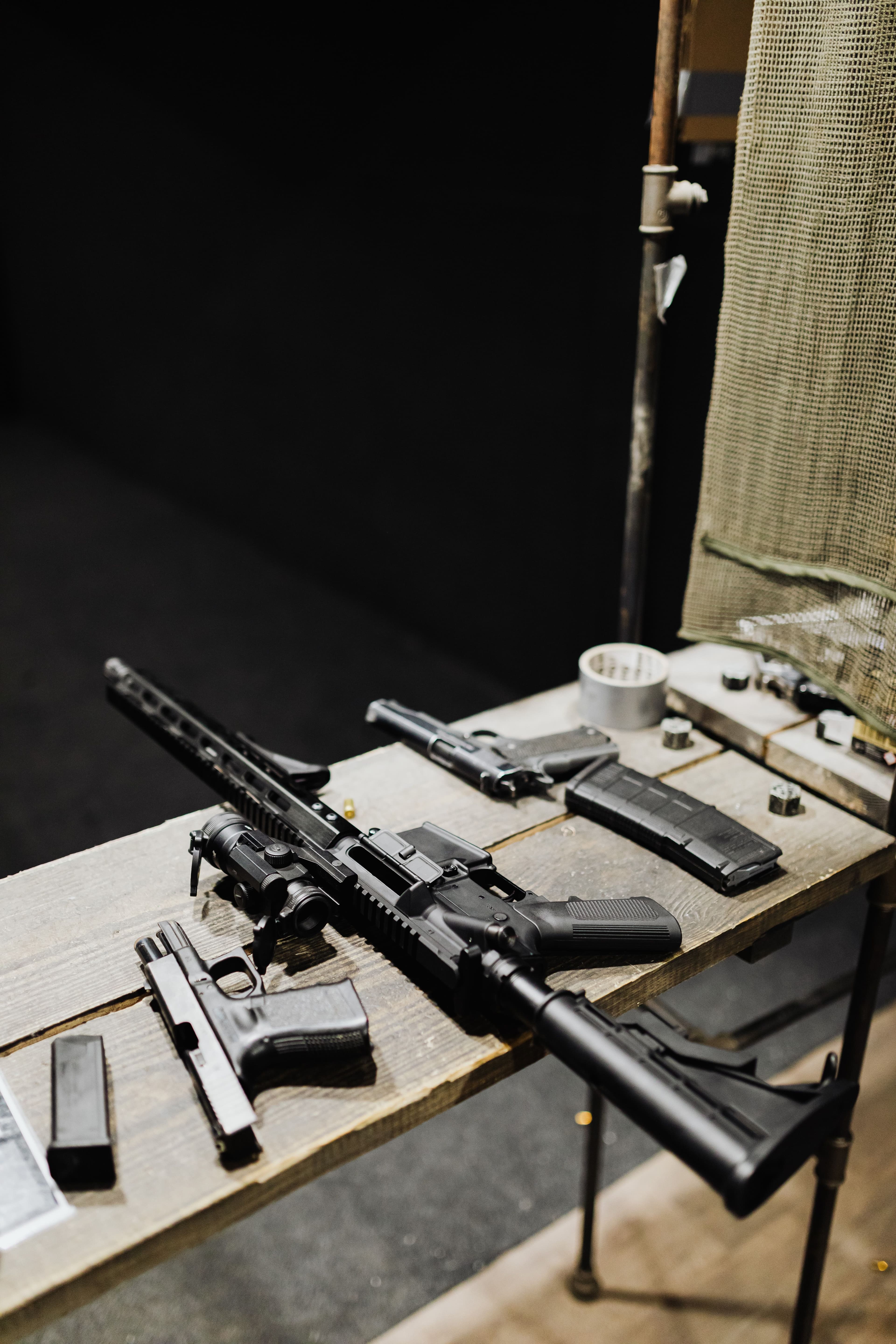 A rifle and handguns displayed on a range table with magazines.