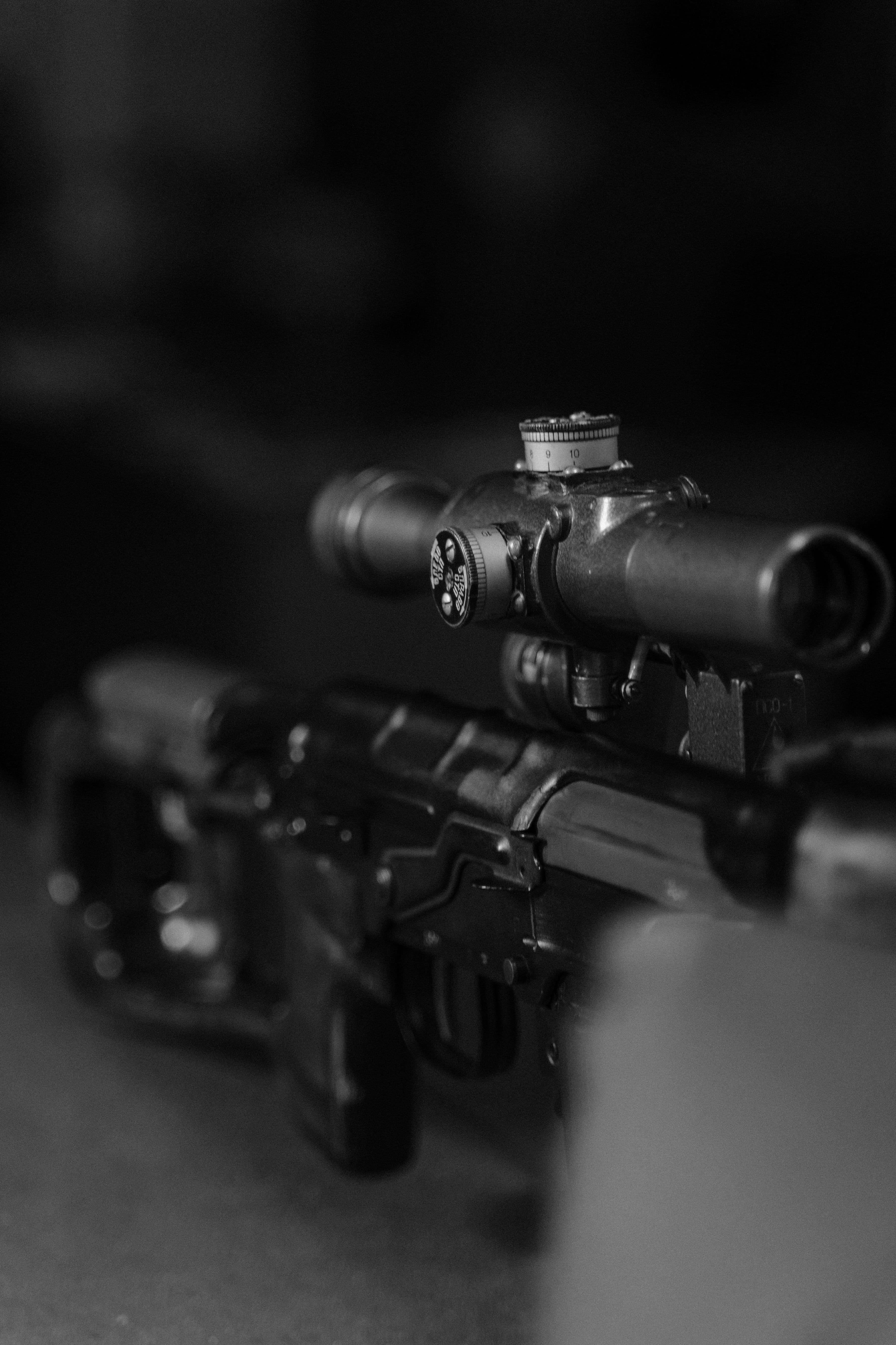 Black and white close-up of a rifle-mounted scope and receiver.