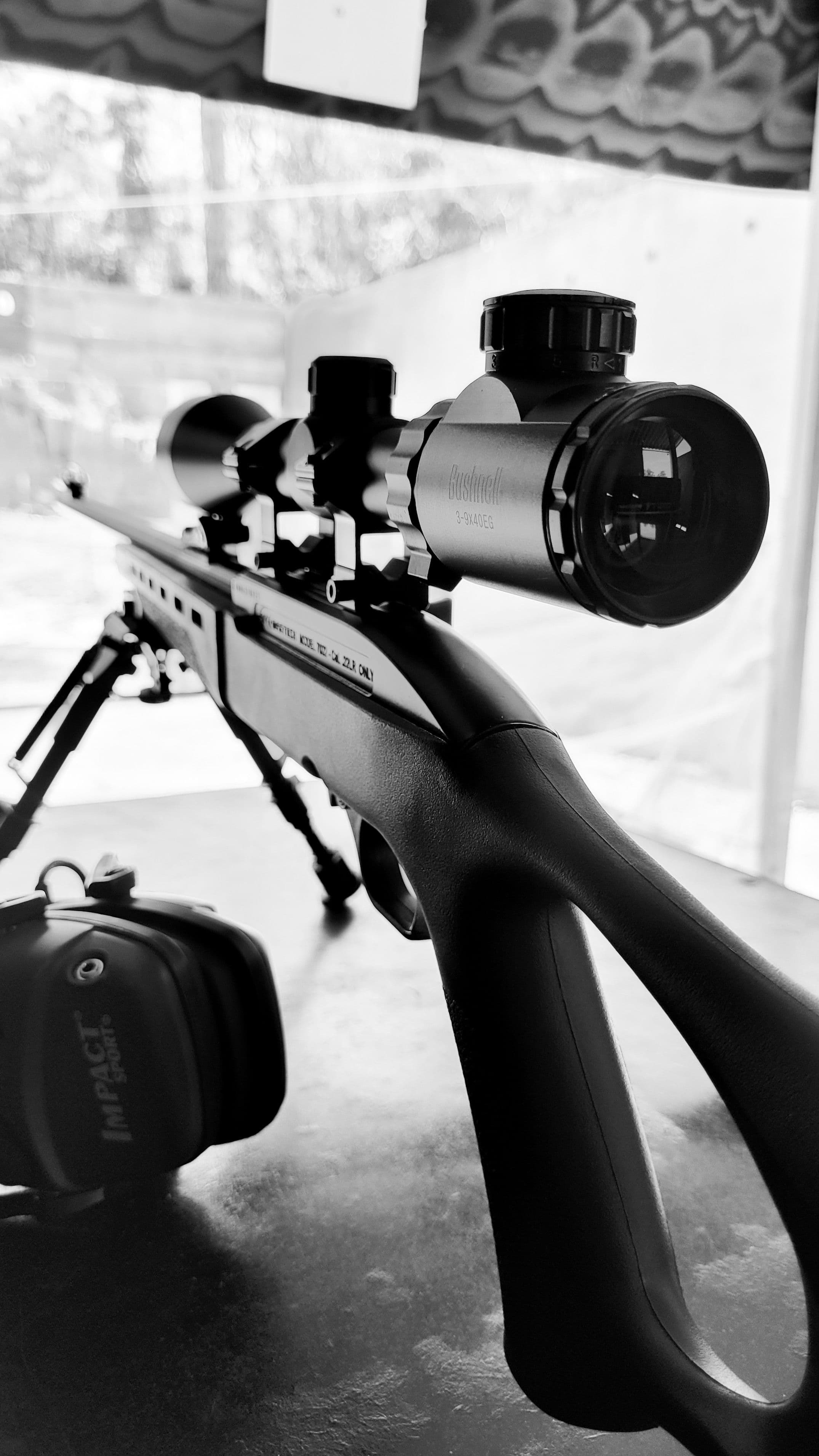 Black and white close-up of a scope mounted on a bolt-action rifle.