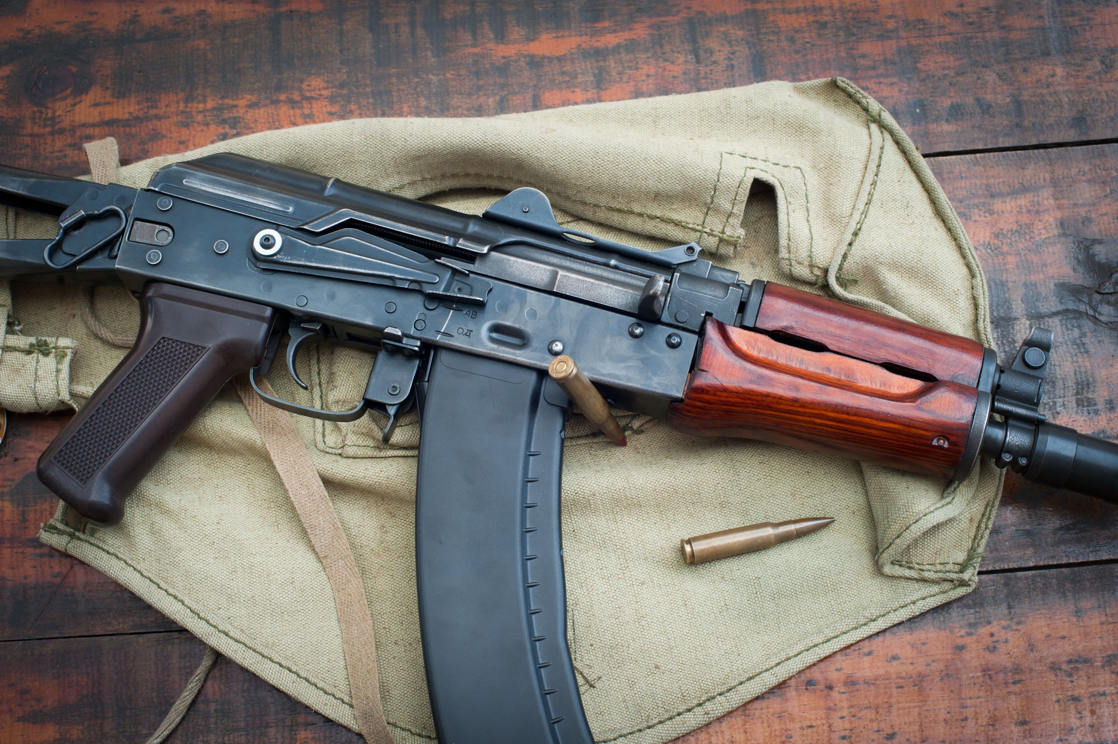 Close-up of a rifle with wood furniture and a loaded curved magazine.