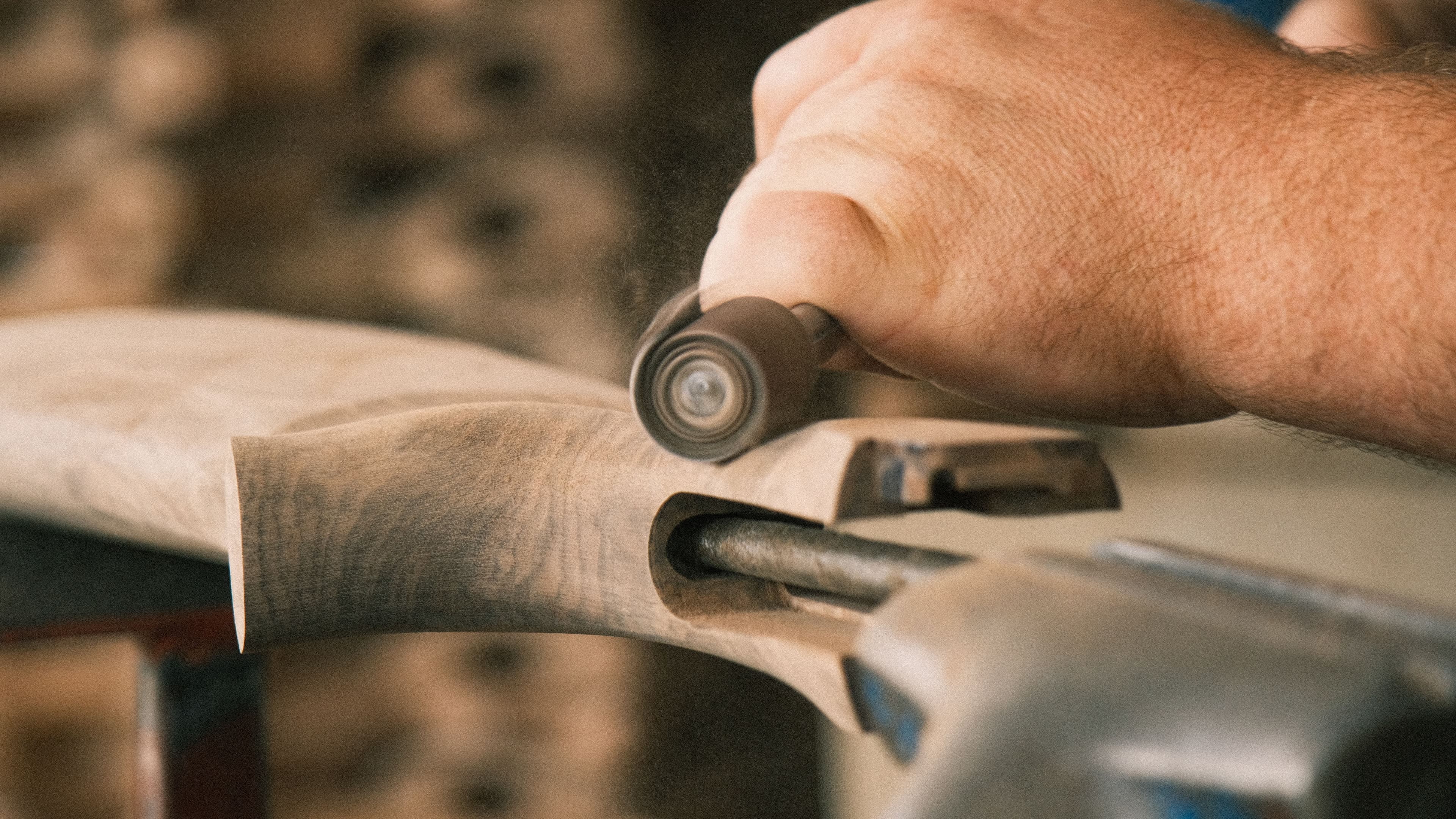 Close-up of hands sanding a wooden rifle stock secured in a vise.