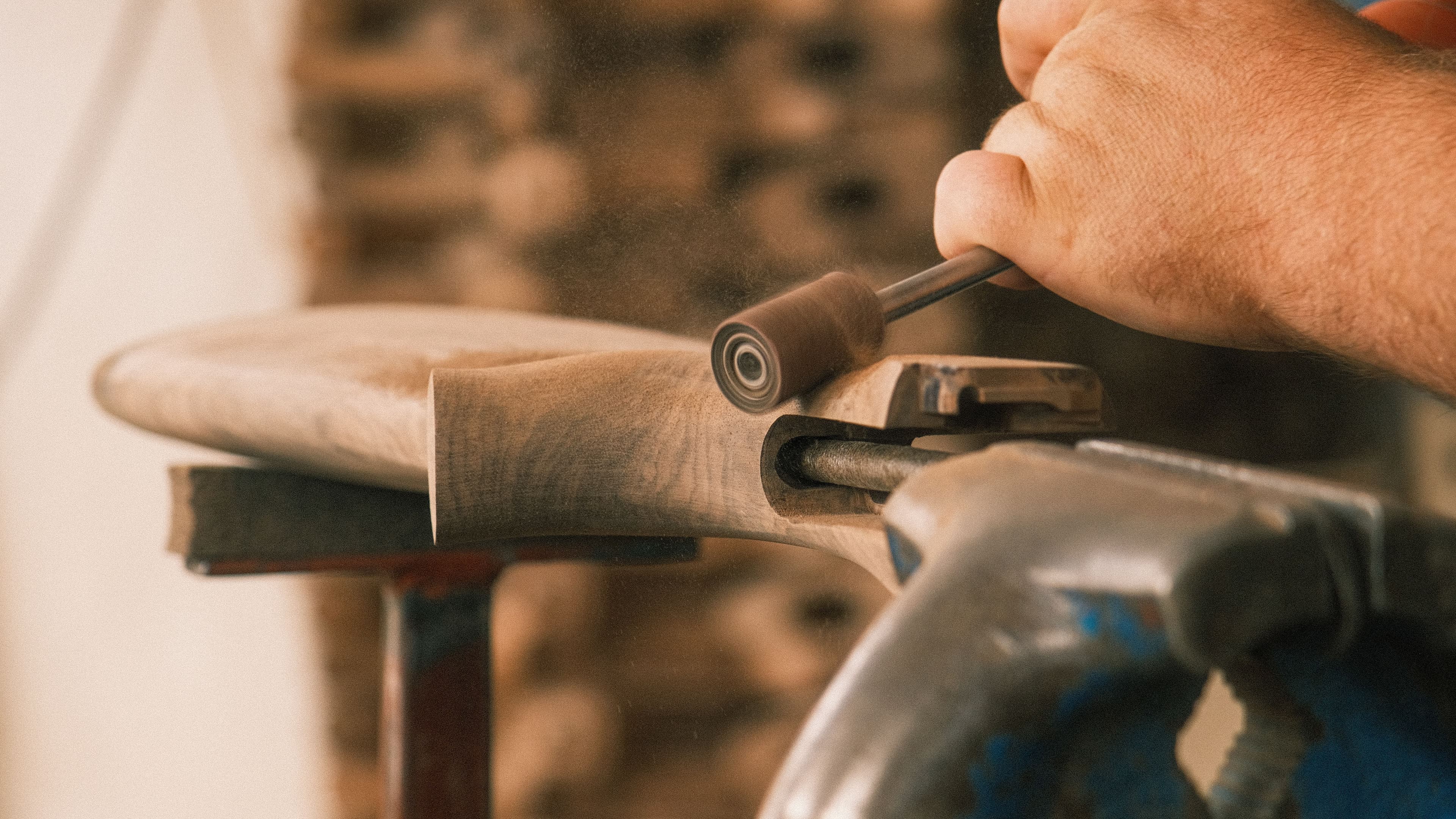 Craftsman shaping a wooden gunstock by hand with a sanding tool.
