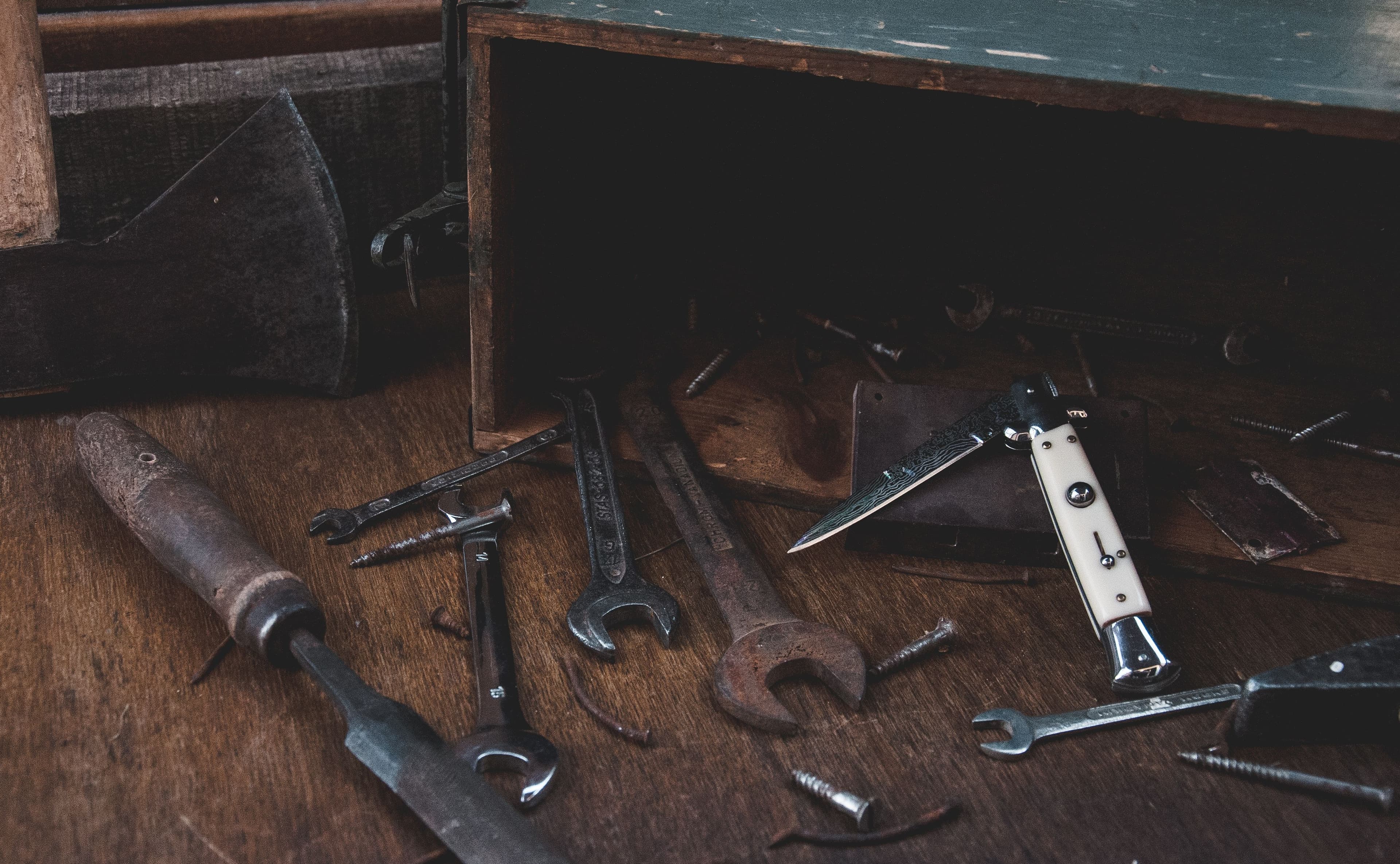 Vintage wrenches and a folding pocketknife arranged on a wooden workbench.