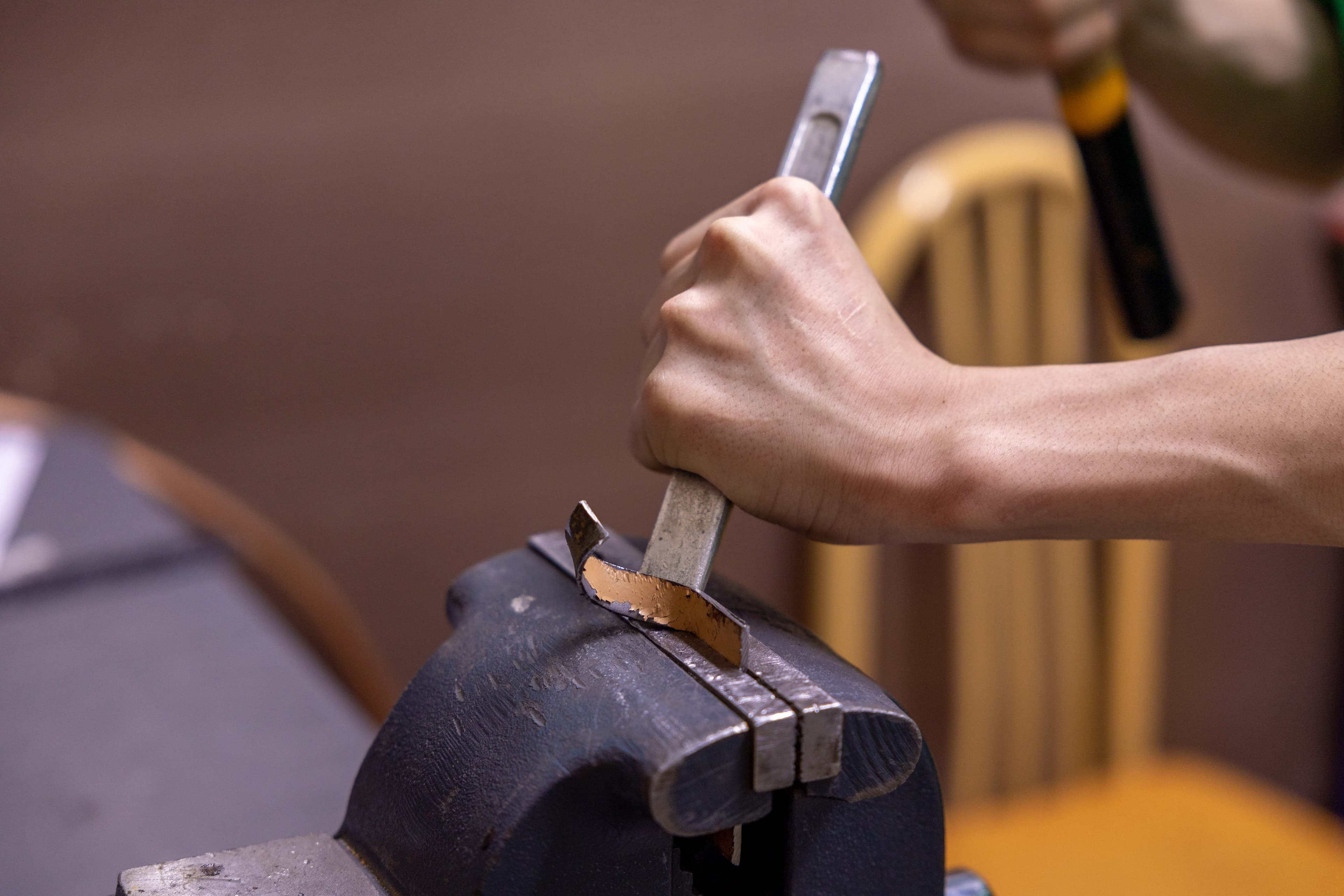 Close-up of a hand filing a metal part clamped in a bench vise.
