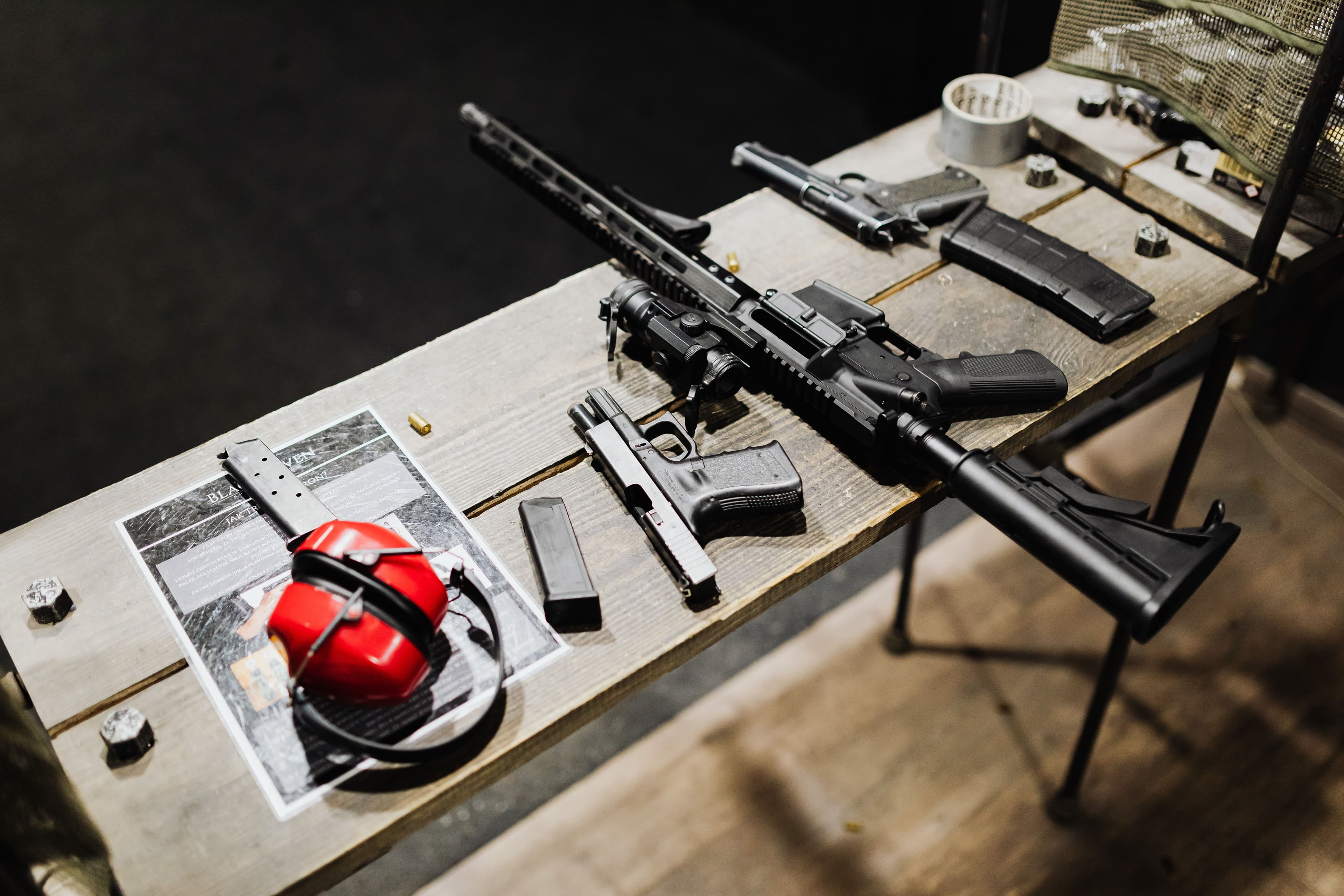 A rifle, pistols, magazines, and ear protection laid out on a range table.