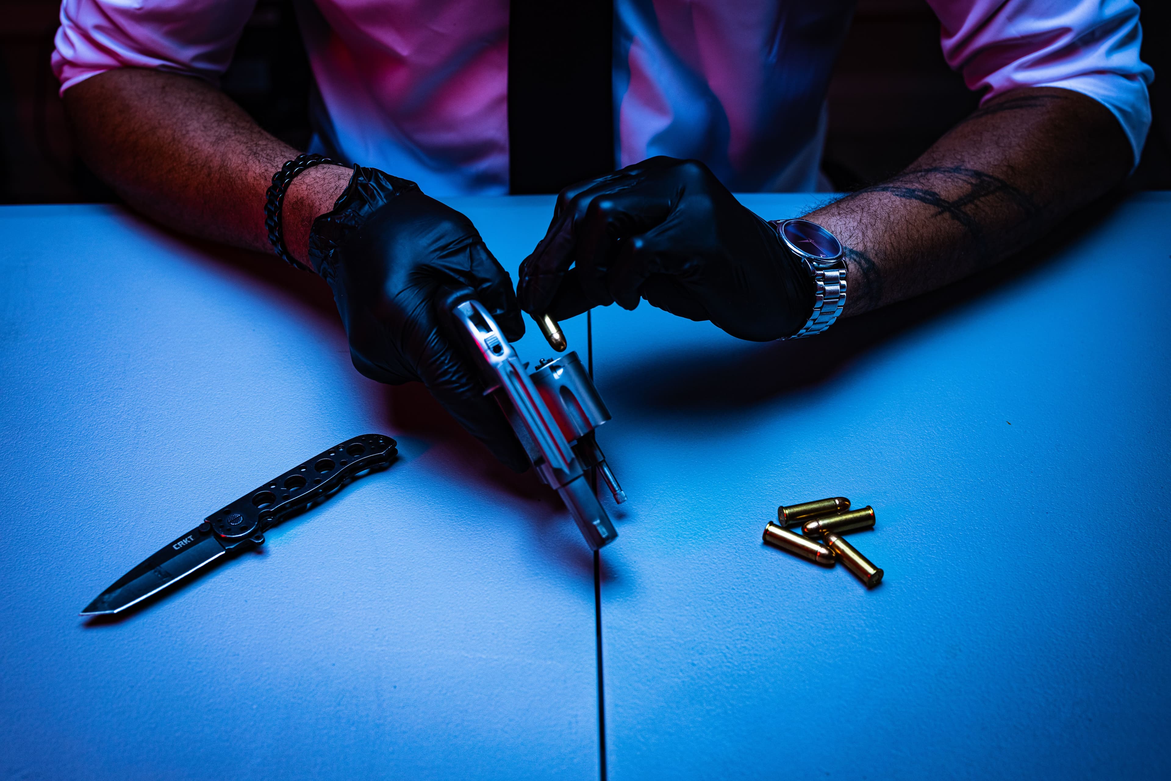 Gloved hands loading a revolver under dramatic lighting.