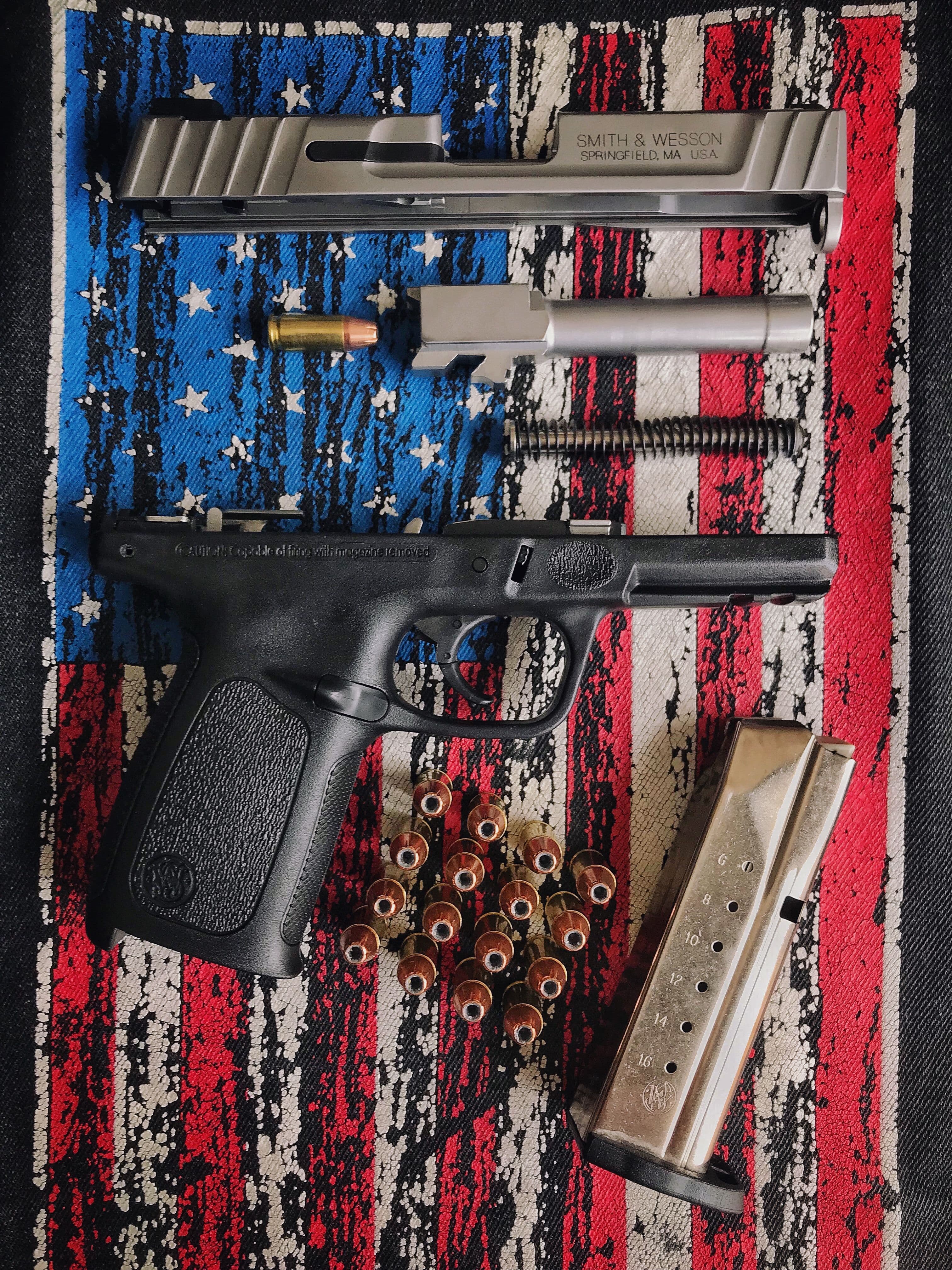 Disassembled pistol slide, barrel, and frame arranged with loose ammunition.